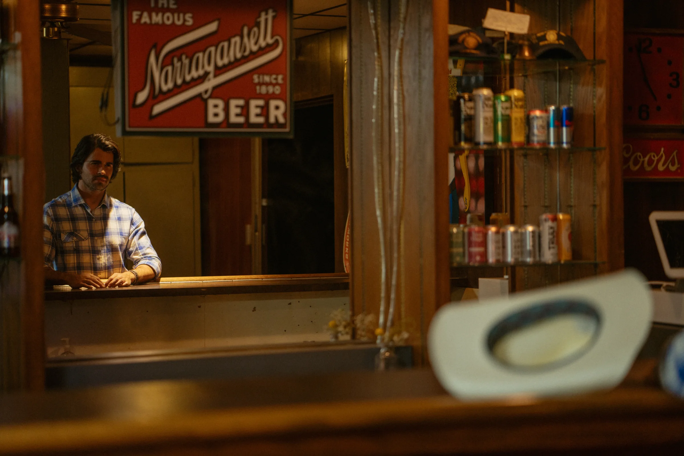 Gigio Teixeira diante do balcão de um bar country em retrato de luz quente