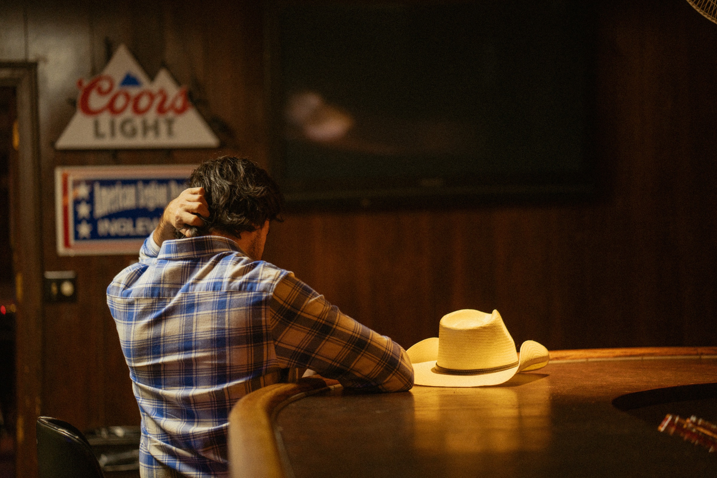 Gigio Teixeira de costas em um bar de Nashville, com o chapéu sobre o balcão